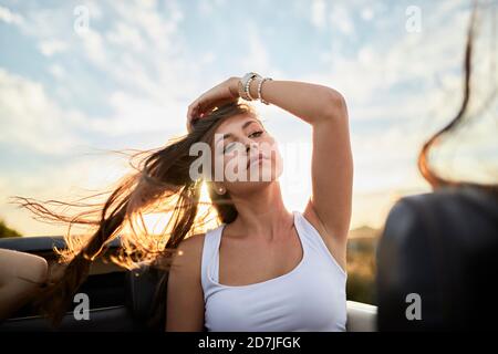 Junge Frau schaut weg, während sie im Cabrio gegen den Himmel sitzt Bei Sonnenuntergang Stockfoto