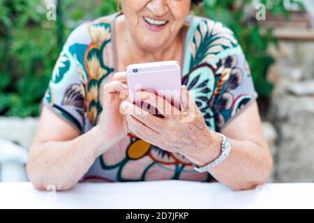 Nahaufnahme einer älteren Frau mit Mobiltelefon am Tisch während Sitzen im Hof Stockfoto