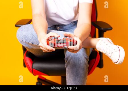 Frau, die hinter einem Spielstuhl in ihren Händen sitzt und rot hält Gamepad auf gelbem Hintergrund Stockfoto