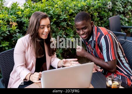 Lächelndes junges Paar, das auf den Laptop schaut, während es am Tisch sitzt Im Café Stockfoto