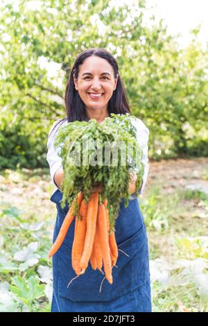 Lächelnde reife Frau hält frisch geerntete Karotten aus dem Gemüsegarten Stockfoto