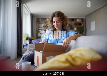 Frau, die Box öffnet, während sie zu Hause auf dem Sofa sitzt Stockfoto