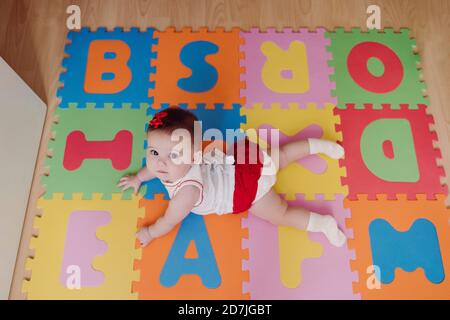 Nettes Baby Mädchen liegt auf bunten Puzzle-Spielmatte zu Hause Stockfoto