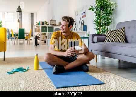 Lächelnder junger Mann, der das Mobiltelefon am Stativ hält Zu Hause sitzen Stockfoto