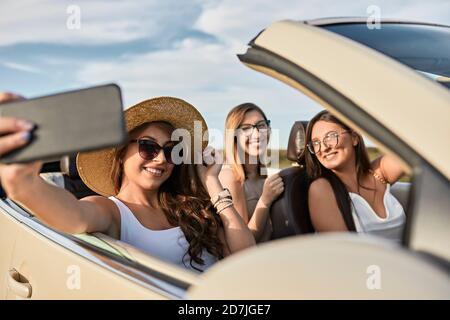 Freunde, die Selfie auf dem Smartphone machen, während sie unterwegs sind Sitzen in einem Luxusauto Stockfoto