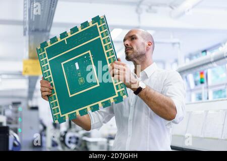 Selbstbewusster reifer männlicher Techniker mit Blick auf große Leiterplatte während Untersuchung in beleuchteter Fabrik Stockfoto