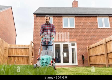 Mittlerer Erwachsener Mann mit Rasenmäher für das Mähen im Hinterhof Stockfoto