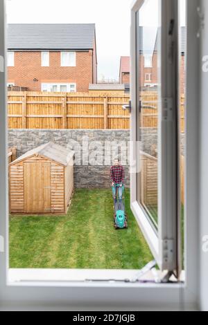 Offenes Fenster mit Mann mäht Hinterhof im Hintergrund Stockfoto