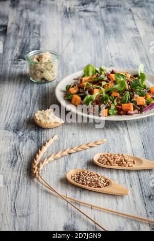 Teller vegetarischer Salat mit Süßkartoffeln und Wildreis Und zwei Holzlöffel mit Grüner Dinkel und Quinoa Stockfoto