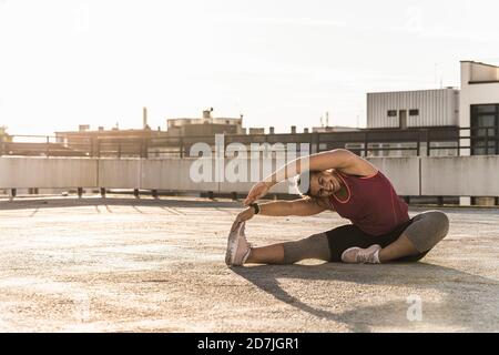 Lächelnde junge Frau mit erhobenen Armen trainieren auf der Terrasse gegen Klarer Himmel in der Stadt Stockfoto
