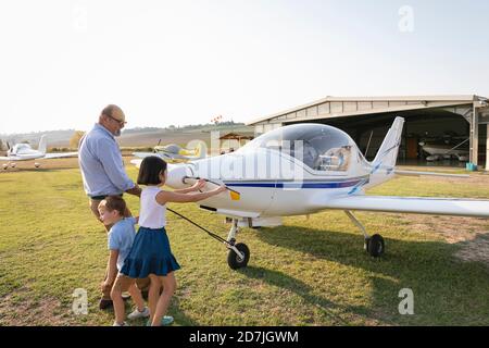 Kinder und Großvater ziehen das Flugzeug aus dem Hangar Stockfoto