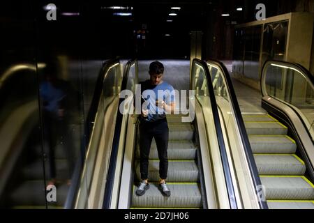 Junger Mann, der Smartphone benutzt, während er das digitale Tablet anhält Rolltreppe an der U-Bahn Stockfoto
