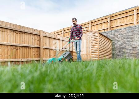 Mann mit Rasenmäher beim Gehen im Hinterhof Stockfoto