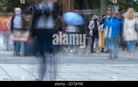 Stuttgart, Deutschland. Oktober 2020. Drei Passanten mit Mund- und Nasenschutz stehen im Stadtzentrum, während Menschen um sie herum vorbeiziehen. (Wischen Effekt durch lange Zeit Exposition) Kredit: Sebastian Gollnow/dpa/Alamy Live News Stockfoto