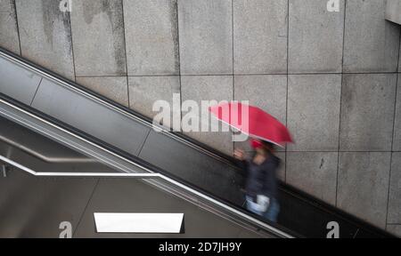 Stuttgart, Deutschland. Oktober 2020. Eine Frau mit einem roten Schirm und einem roten Mund-und-Nase-Protektor reitet auf einer Rolltreppe. (Wischen Wirkung der langen Exposition) Kredit: Sebastian Gollnow/dpa/Alamy Live News Stockfoto