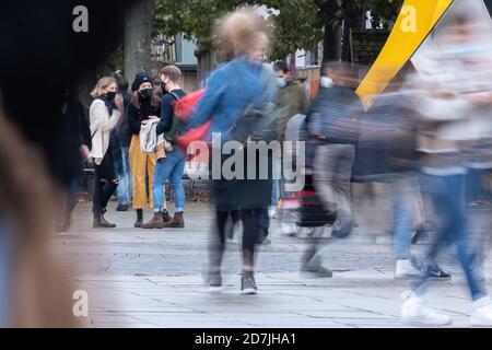 Stuttgart, Deutschland. Oktober 2020. Drei Passanten mit Mund- und Nasenschutz stehen im Stadtzentrum, während Menschen um sie herum vorbeikommen. (Wischen Effekt durch lange Zeit Exposition) Kredit: Sebastian Gollnow/dpa/Alamy Live News Stockfoto