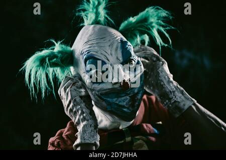 Nahaufnahme eines verstörenden bösen Clowns, mit grünen Haaren, mit einem schmutzigen roten Kostüm, einer schmutzigen Fliege und schmutzigen und blutigen Handschuhen, an- oder ausziehen Stockfoto