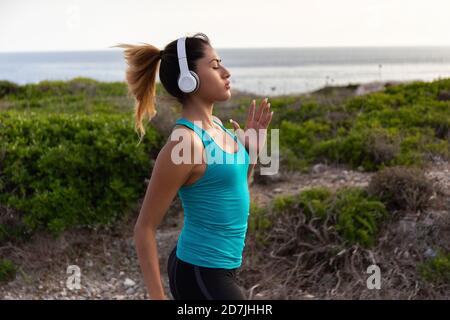 Junge Lateinerin, die Musik hört, während sie in der Nähe des Meeres joggt Stockfoto