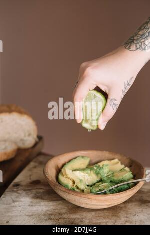 Frau Hand quetscht Limette in Avocado-Salat auf Schneiden gehalten Brett in der Küche Stockfoto