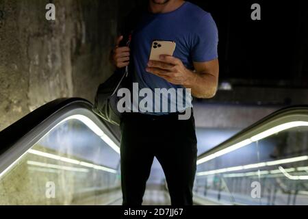 Junger Mann, der Smartphone benutzt, während er mit Rucksack steht Rolltreppe an der U-Bahn Stockfoto