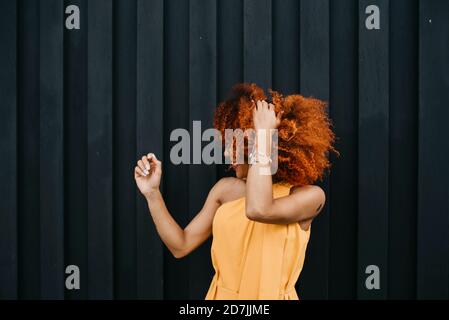 Fröhliche junge Frau schüttelt die Haare, während sie an der Wand steht Stockfoto