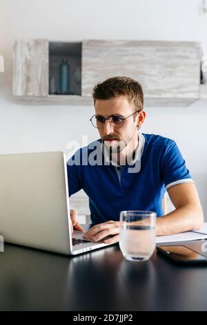 Schöner junger Mann mit Laptop, während Hausaufgaben am Tisch Stockfoto