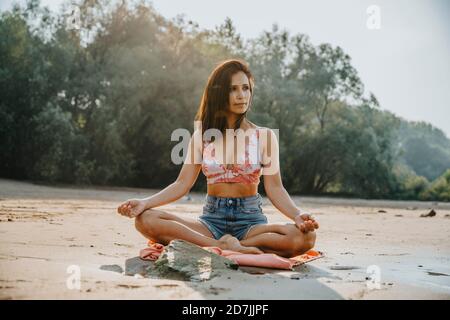 Reife Frau meditiert am Strand an sonnigen Tag Stockfoto