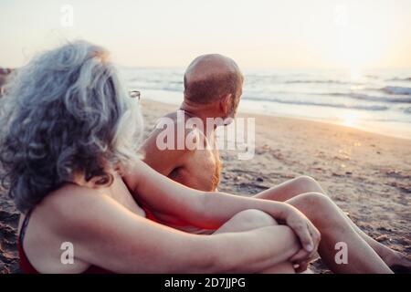 Ältere Paare bewundern den Sonnenuntergang beim Sitzen am Strand Stockfoto