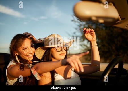 Lächelnde junge Freunde zeigen, während sie im Cabrio sitzen Stockfoto