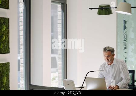 Mann, der am Laptop arbeitete, während er am Schreibtisch im Büro saß Stockfoto