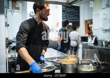 Lächelnder Koch arbeitet mit Mitarbeiter, der Aufträge im Hintergrund entgegennimmt Küche Stockfoto