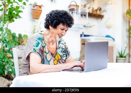 Glückliche ältere Frau mit Laptop auf dem Tisch, während sie sitzt Hof Stockfoto