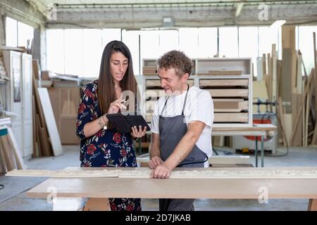 Innenarchitekt, der dem Zimmermann beim Stehen ein digitales Tablet zeigt Werkstatt Stockfoto