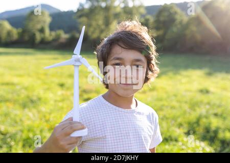 Junge lächelnd, während die Windturbine Spielzeug in der Wiese hält Stockfoto