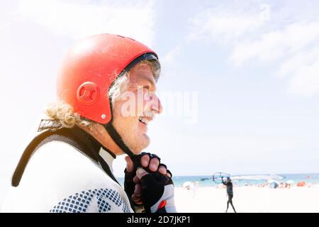 Nahaufnahme eines lächelnden älteren Mannes mit Sporthelm am Strand Gegen den Himmel im Sommer Stockfoto
