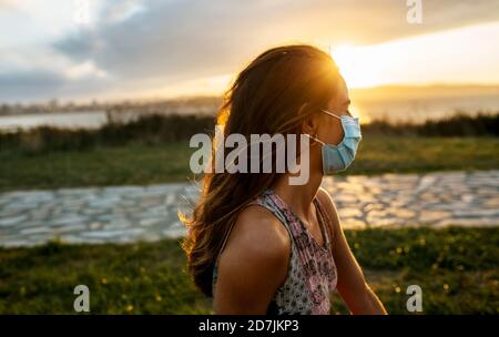 Junge Frau in schützender Gesichtsmaske gegen Himmel während COVID-19 Ausbruch Stockfoto