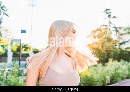 Fröhliche junge Frau schüttelt Haare, während im Park während stehen Sonnenuntergang Stockfoto