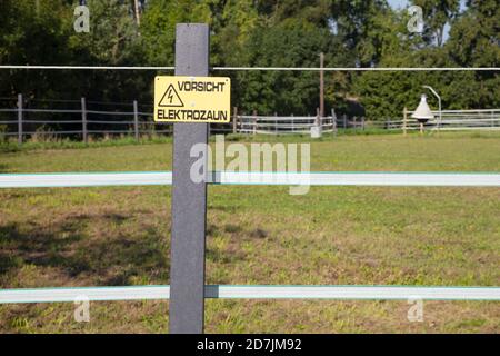 Warnschild am elektrischen Zaun gegen Bäume Stockfoto