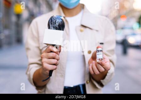 Nahaufnahme einer Reporterin, die eine Maske trägt und dabei eine Impfstoffflasche zeigt Im Freien stehen Stockfoto