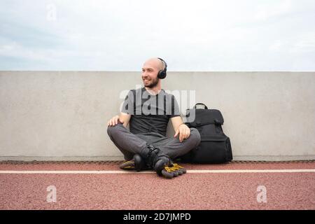 Der Mann trägt Inline-Skates und hört während des Sitzens Musik über Kopfhörer Auf der Brücke Stockfoto