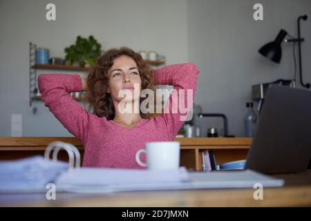 Frau mit den Händen hinter dem Kopf entspannen beim Sitzen am Tisch Zu Hause Stockfoto