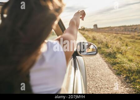 Junge Frau zeigt in Richtung wolkigen Himmel, während sie im Auto sitzt Stockfoto