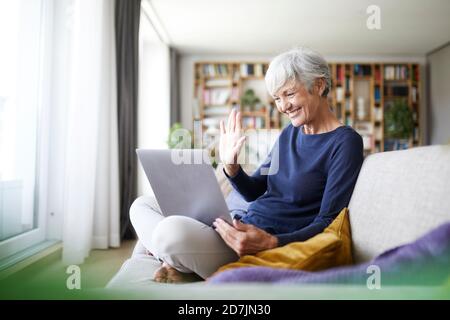 Ältere Frau macht hohe fünf bei Videoanruf während der Verwendung Laptop zu Hause Stockfoto