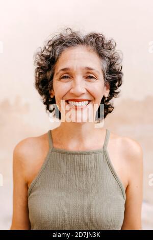 Reife Frau lächelt, während sie gegen die Wand steht Stockfoto