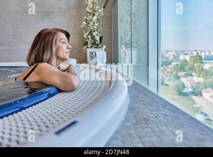 Ältere Frau schaut durch das Fenster, während sie im Swimmingpool liegt Stockfoto