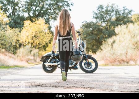 Blonde Frau hält Helm, während zu Fuß in Richtung Motorrad auf der Straße Stockfoto