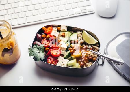 Lunchbox mit frischem veganem Salat auf dem Schreibtisch Vorderseite der Computertastatur Stockfoto
