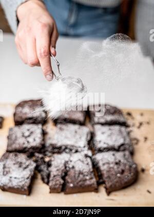 Vertikale Aufnahme eines Bäckers, der eine frisch gebackene Brownies entstaubt Mit Puderzucker Stockfoto