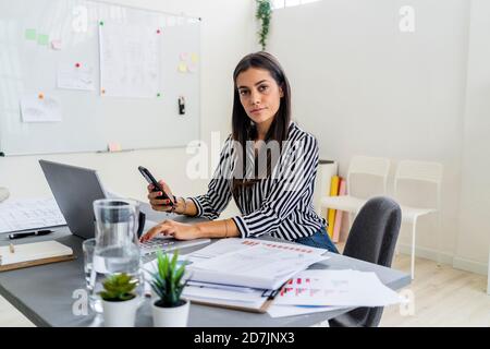 Selbstbewusstes, professionelles Sitzen im weiblichen Design mit drahtlosen Technologien am Schreibtisch Im Büro Stockfoto