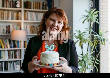 Frau hält Kuchen mit der Kerze Nummer 50 im Stehen Zu Hause Stockfoto